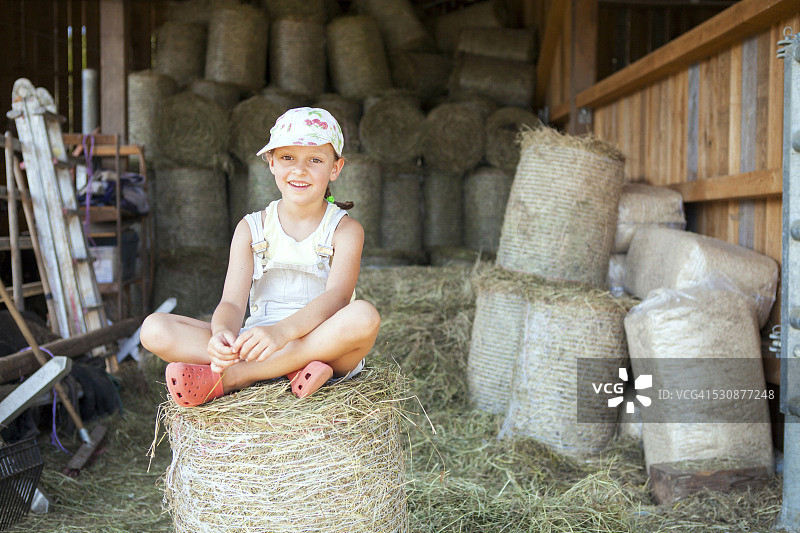 小女孩坐在马厩里的干草捆上图片素材