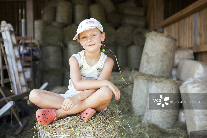 小女孩坐在马厩里的干草捆上图片素材