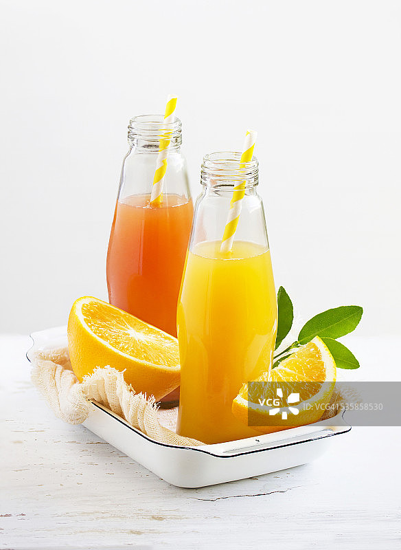 瓶装柑橘果汁与饮用吸管旁边的切柑橘类水果家庭堆放在白色的背景。图片素材