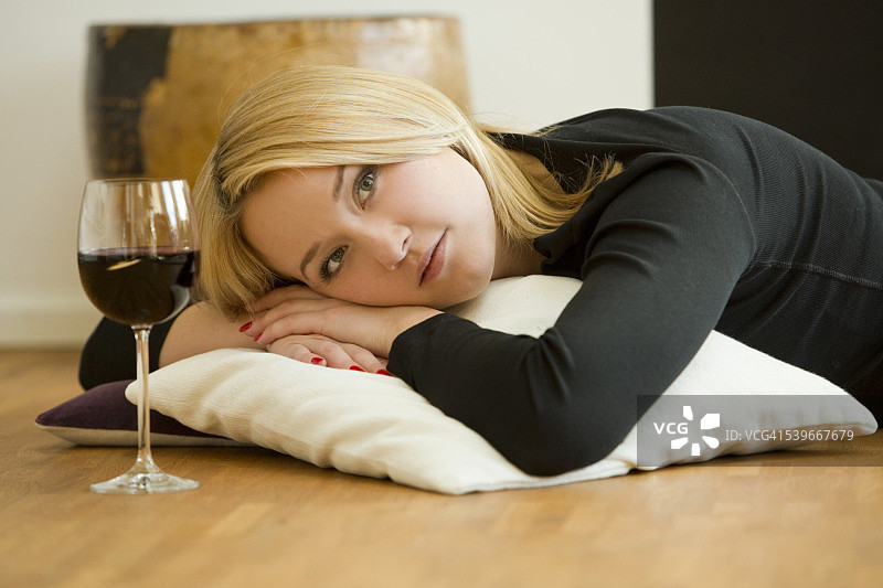 金发年轻女子躺在地板上，手里拿着一杯红酒图片素材