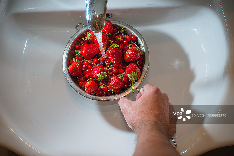 男人在厨房水槽洗涤浆果的高角度视图图片素材