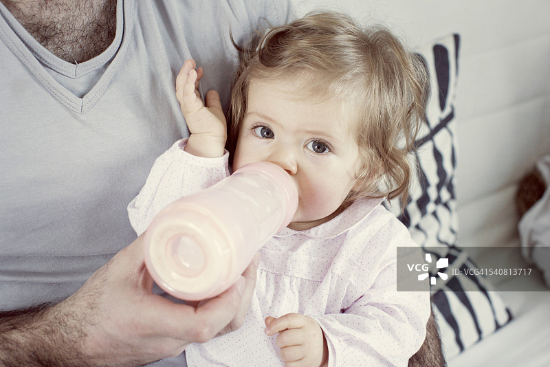 女婴坐在父亲的腿上，喝着奶瓶里的水图片素材
