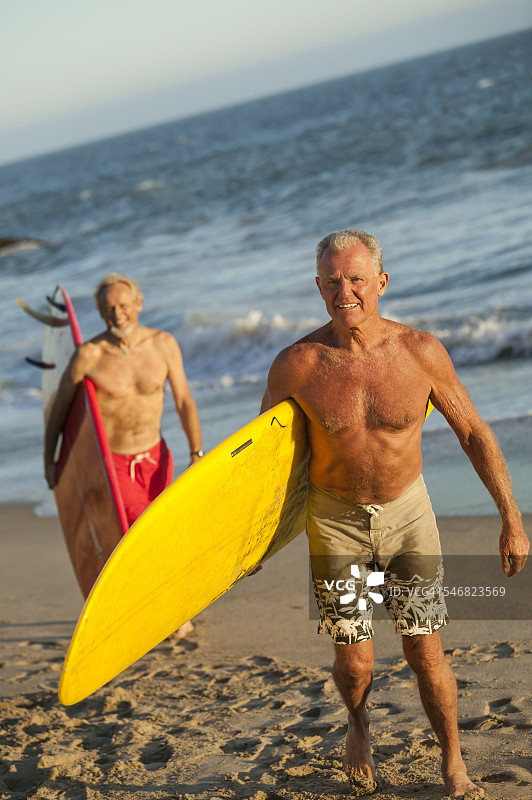 在海滩上扛着冲浪板的老年人图片素材