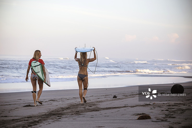 印度尼西亚，巴厘岛，两名妇女扛着冲浪板在海滩上图片素材