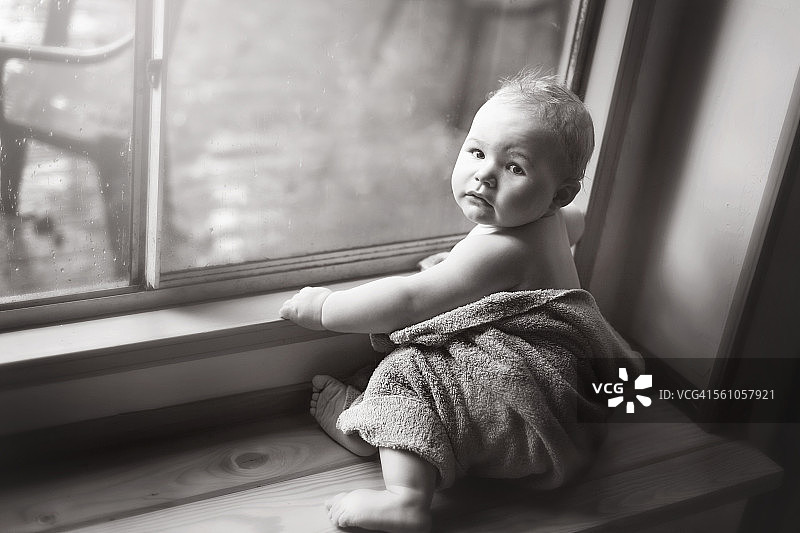 婴儿裹着毛巾坐在靠窗的座位上图片素材