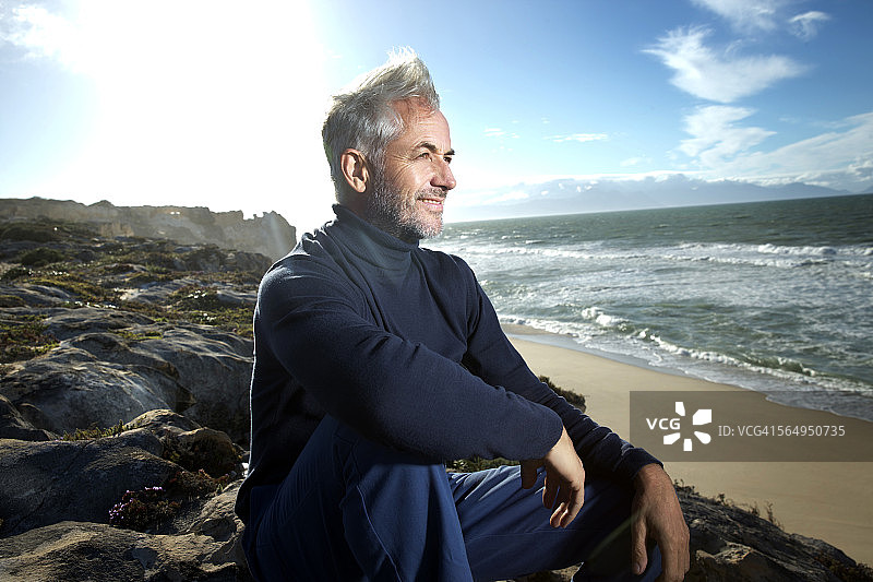南非，一名男子微笑着坐在海滩上的岩石上图片素材