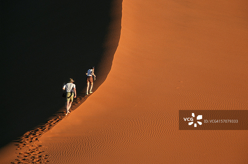 两个徒步旅行者正在爬一座红沙丘图片素材