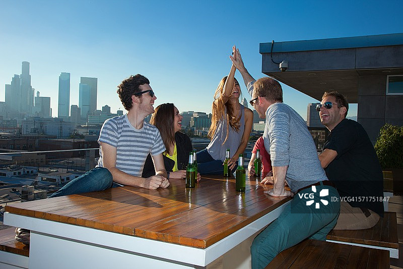 六个成年人朋友在美国洛杉矶天际线的屋顶酒吧喝啤酒图片素材