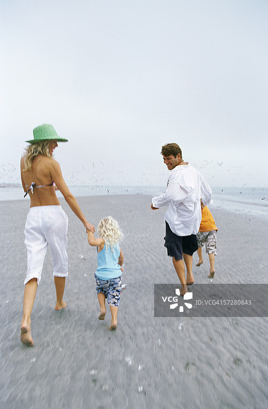 后视图的父母和他们的孩子走在海滩上图片素材