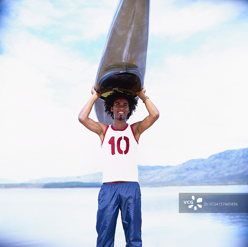 一个年轻人头上顶着皮划艇站在岸边的肖像图片素材