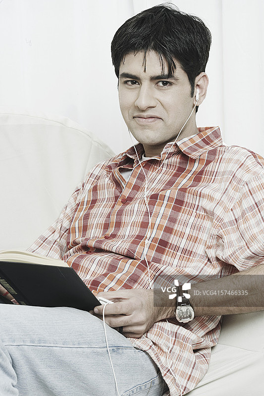 一个年轻人的肖像，膝上放着一本书，正在听MP3图片素材