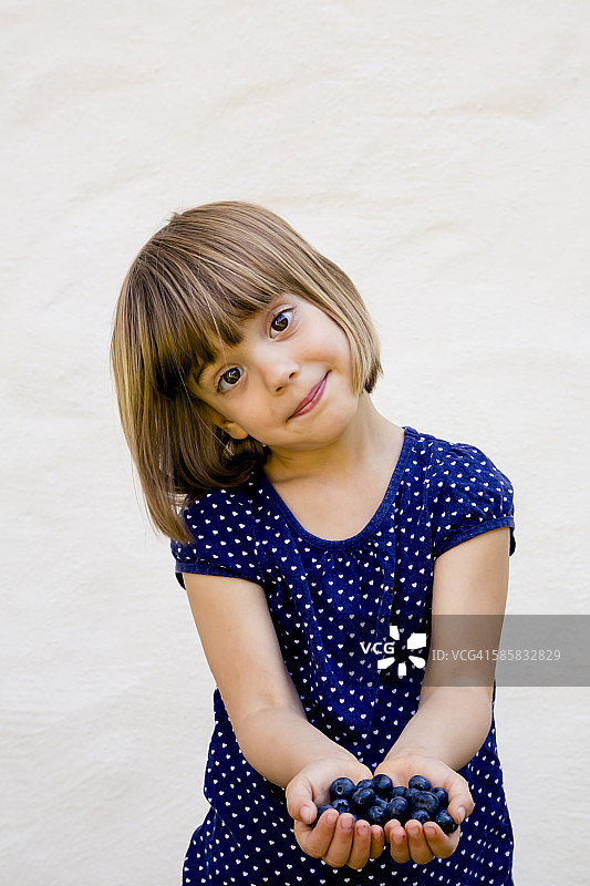 小女孩拿着两把蓝莓的画像图片素材