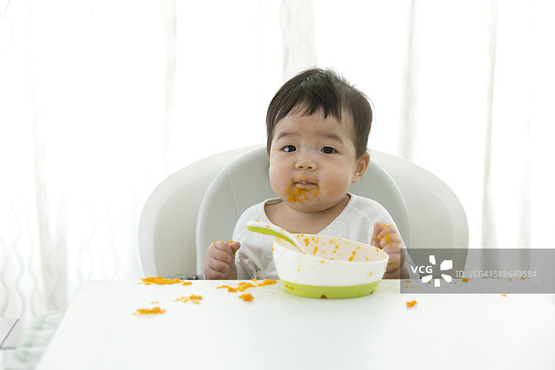 亚洲婴儿学习自我喂养。图片素材