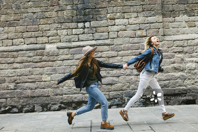 西班牙巴塞罗那，两个年轻女子在城市里手拉手奔跑图片素材