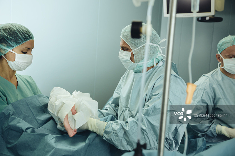 外科医生将剖腹产后的新生儿交给手术室护士图片素材