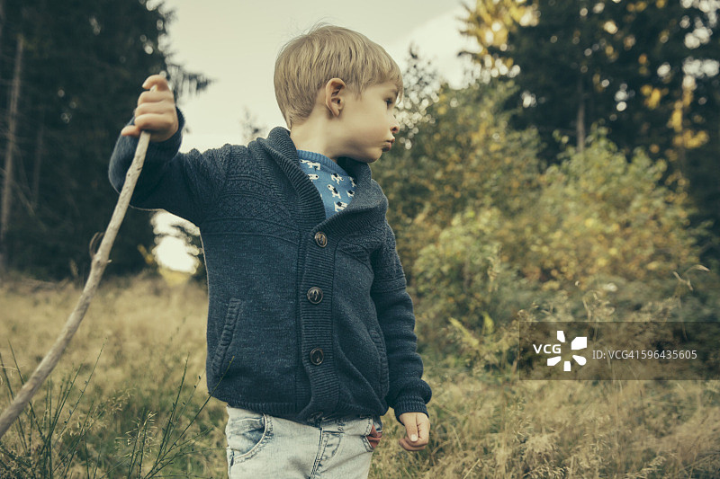小男孩探索森林，用他的棍子在草地上行走图片素材