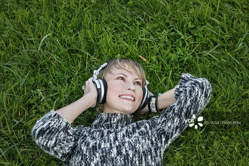 年轻女子戴着耳机躺在草地上图片素材