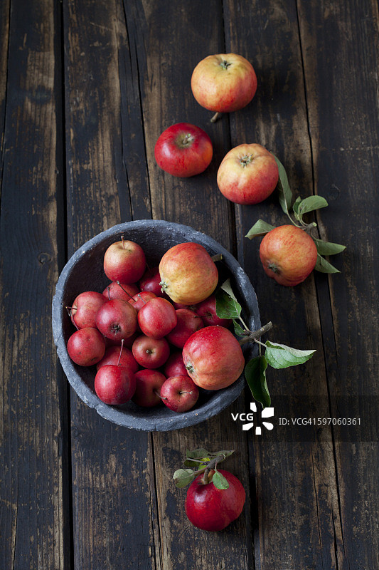 一碗不同种类的红苹果放在深色的木头上图片素材