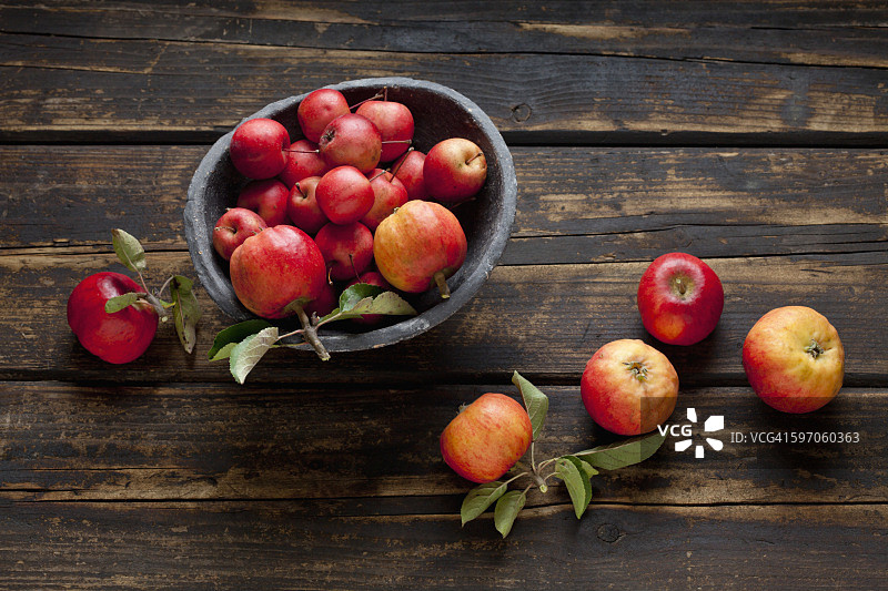 一碗不同种类的红苹果放在深色的木头上图片素材
