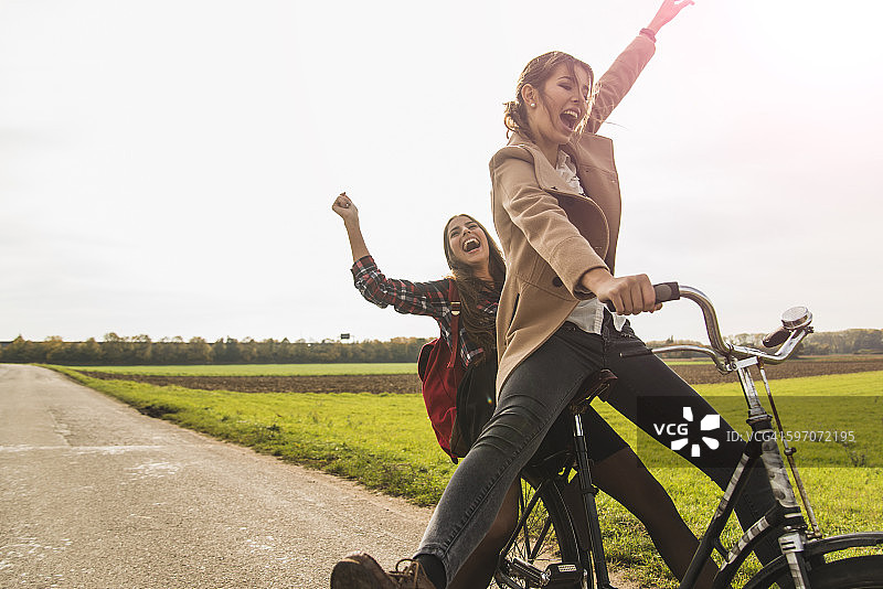 两个精力充沛的年轻女子在乡村风景中共享一辆自行车图片素材