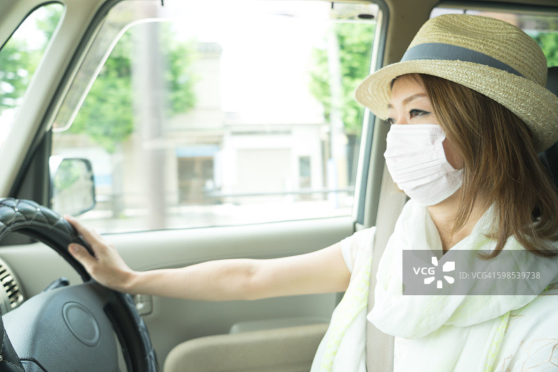 快乐的日本妇女驾驶着汽车，戴着防污染口罩图片素材