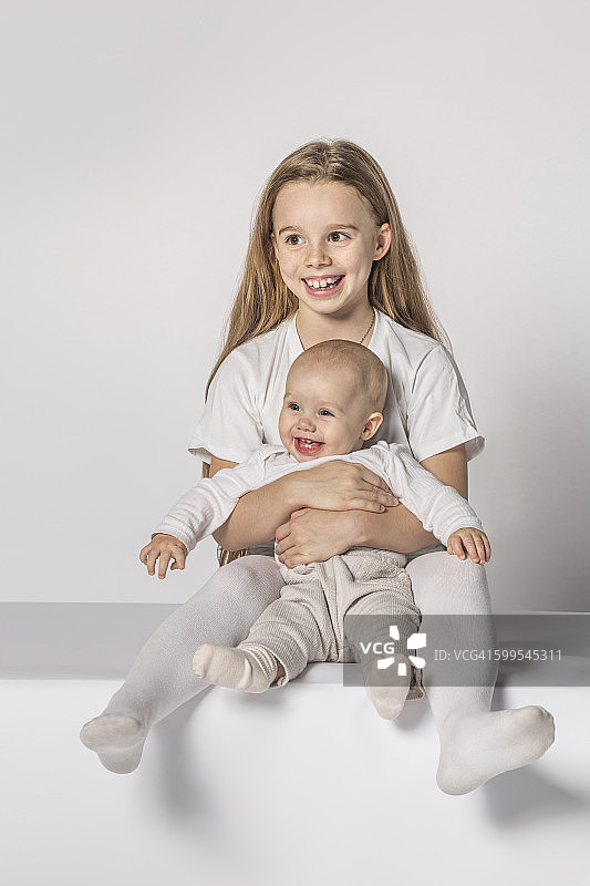 快乐的小女孩和妹妹坐在白色的背景下图片素材