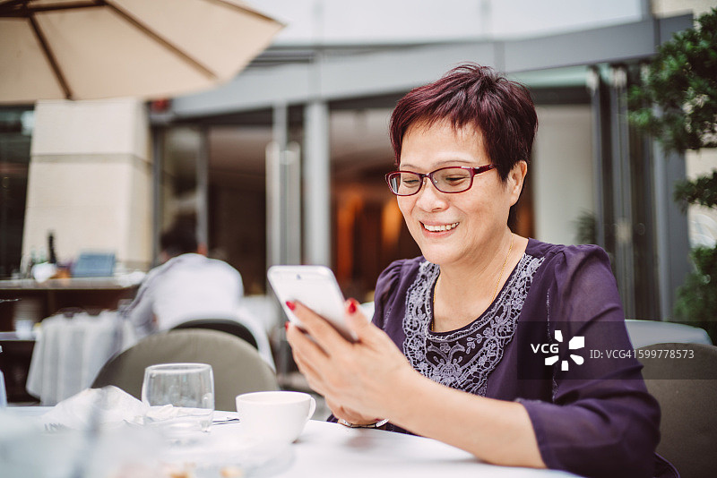 在户外咖啡馆使用智能手机的中年妇女图片素材