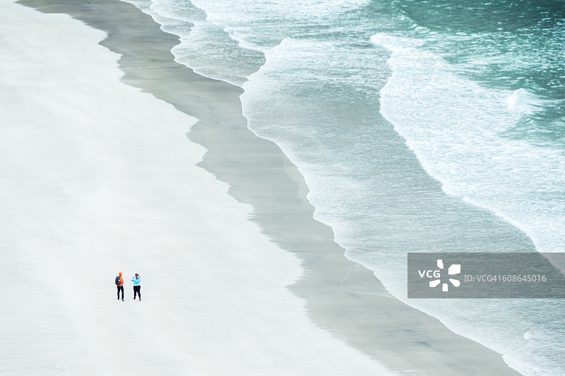 两名徒步旅行者俯瞰挪威罗浮敦海滩上的海浪图片素材