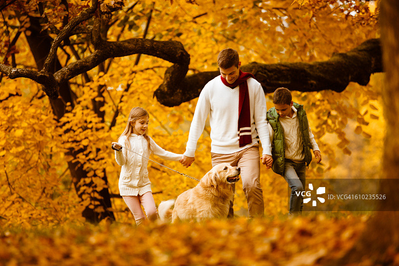 父亲和孩子们带着他们的狗在秋天的公园散步图片素材