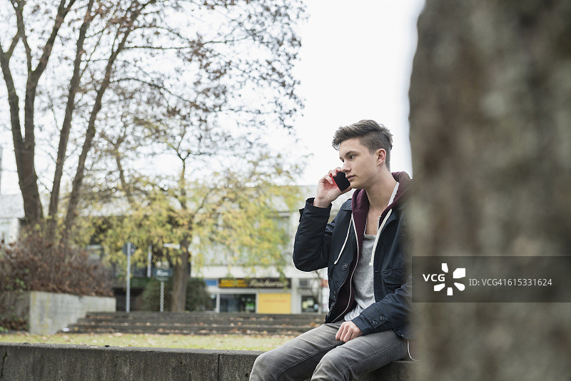 年轻男子坐在窗台上打电话，慕尼黑，巴伐利亚，德国图片素材
