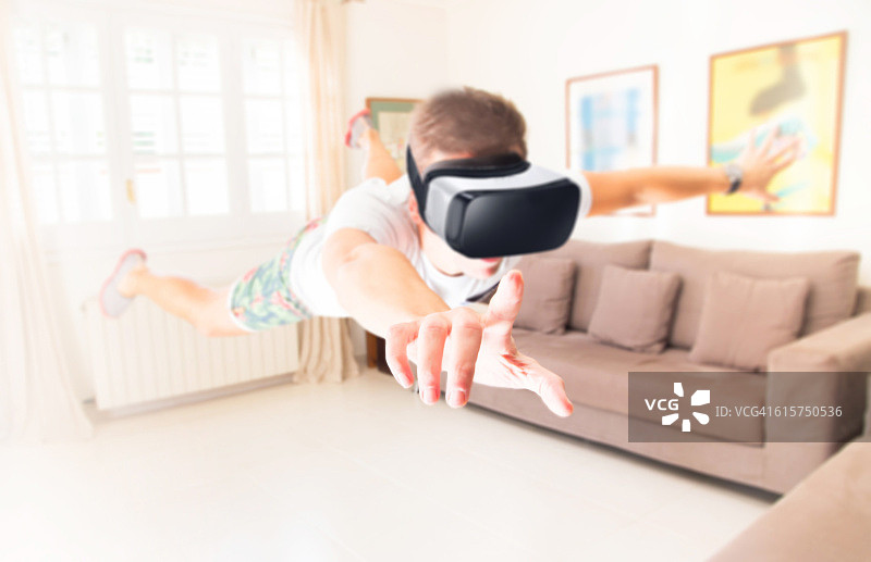 一个人悬浮在明亮的家庭客厅里，使用虚拟现实耳机，体验新技术，并沉浸在另一个世界。虚拟现实头盔是社交交流和娱乐的未来。图片素材