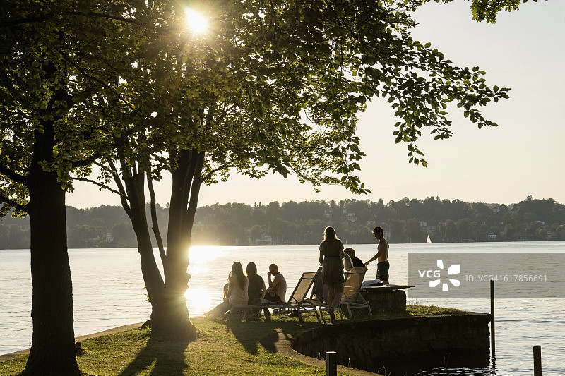 德国巴伐利亚，日落时分，一群年轻的朋友在湖边聚会。图片素材