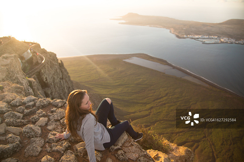女孩坐在兰萨罗特火山岛与美丽的日落光从顶部的视角在岛上旅行假期。图片素材