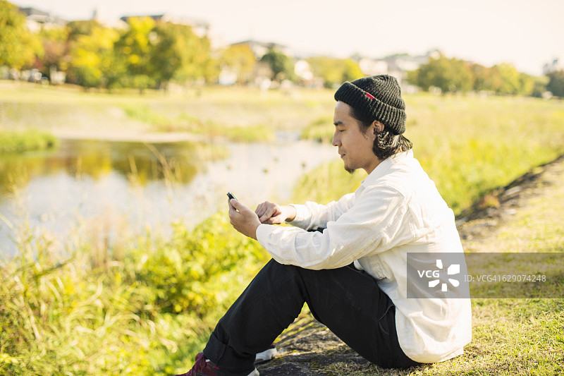 年轻的成年男子在河边使用智能手机图片素材