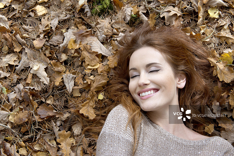 一个迷人的年轻女子躺在森林的地面上，周围是树叶图片素材