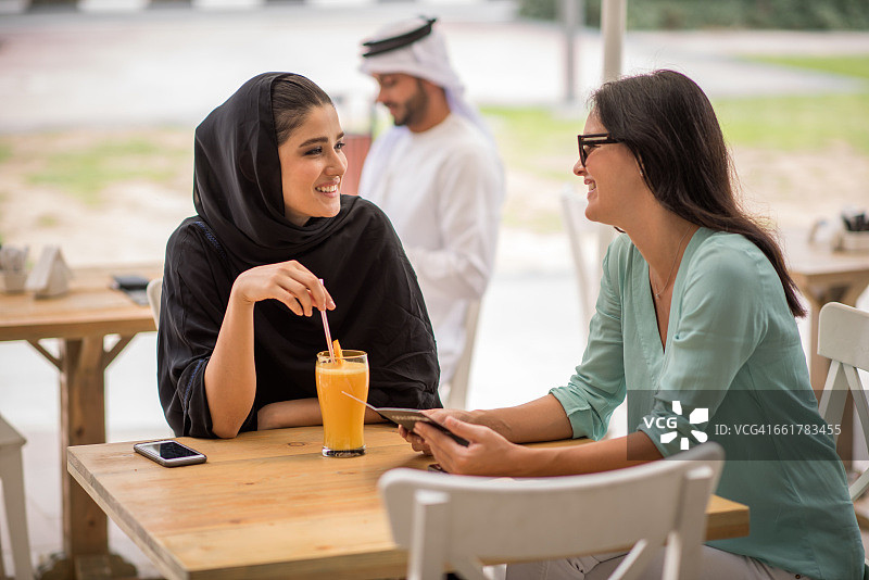 身穿传统服饰的年轻中东女子在阿拉伯联合酋长国迪拜的咖啡馆与女性朋友交谈图片素材