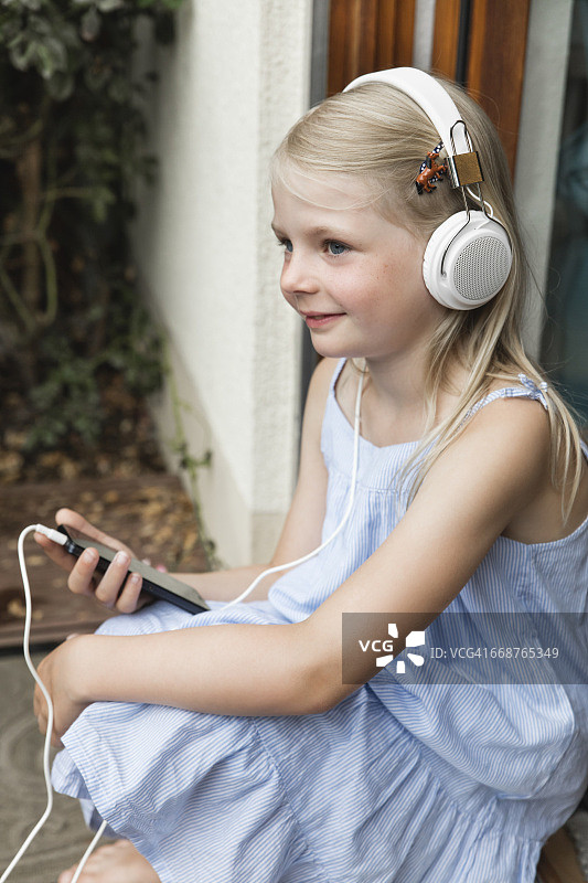 微笑的小女孩听音乐耳机和智能手机图片素材