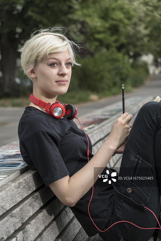 戴着耳机在公园长椅上画的年轻女子肖像图片素材