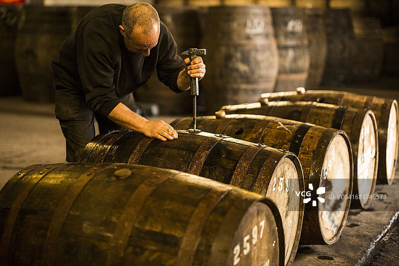 在威士忌酒厂，男工人正在打开木制威士忌酒桶图片素材