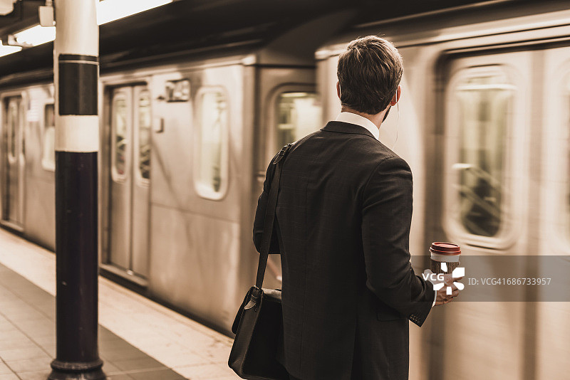 年轻的商人手拿一次性杯子在地铁站站台候车图片素材