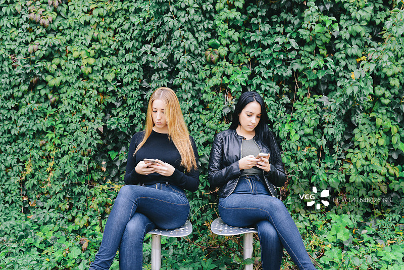 两个年轻的女人坐在一起用手机图片素材