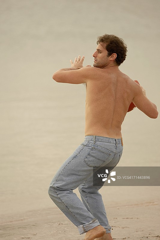 一个中年男人在沙滩上扔橄榄球的后视图图片素材