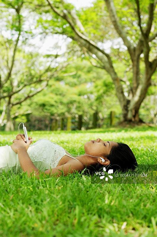 年轻女子躺在草地上，戴着耳机听音乐图片素材