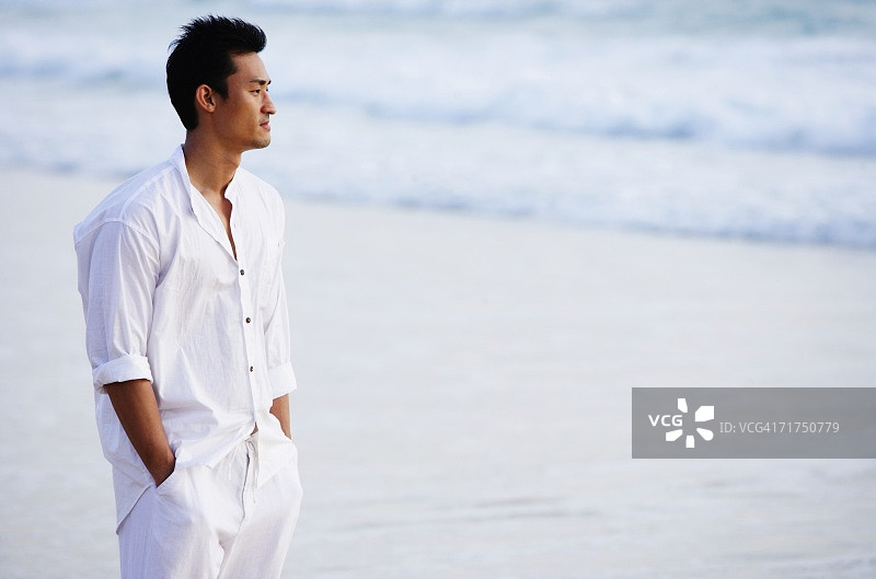 一个男人站在沙滩上，手插在口袋里，看向别处图片素材