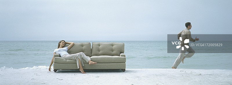 在海滩上，女人躺在沙发上，男人跑开了图片素材