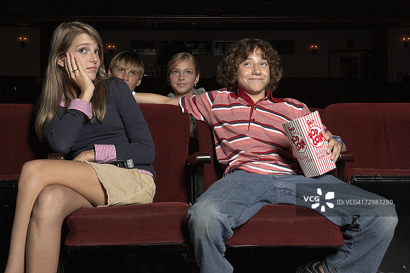 一对青少年情侣坐在电影院的大礼堂里图片素材
