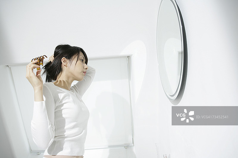 一个拿着发夹看着镜子的年轻女人的侧影图片素材