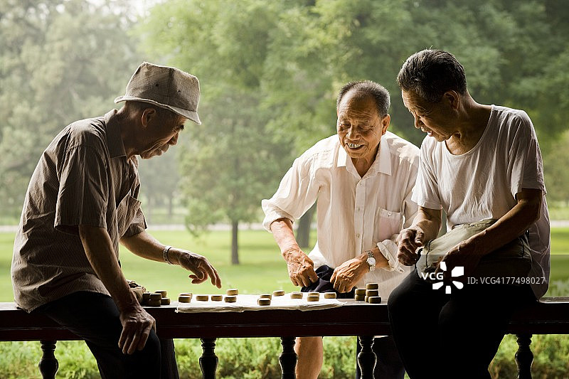 三个男人在户外微笑着玩棋盘游戏图片素材