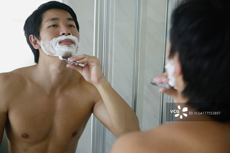男人看着镜子，刮着胡子图片素材