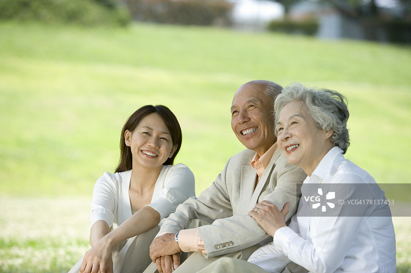 年轻女子与老夫妇微笑着坐在草坪上，不同的焦点图片素材